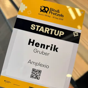 A hand holding the startup badge of Henrik Gruber, Amplexio, with a QR code