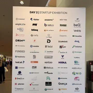 Wall reading “Day 2 | Startup Exhibition” with the logos of all exhibiting startups, including Amplexio
